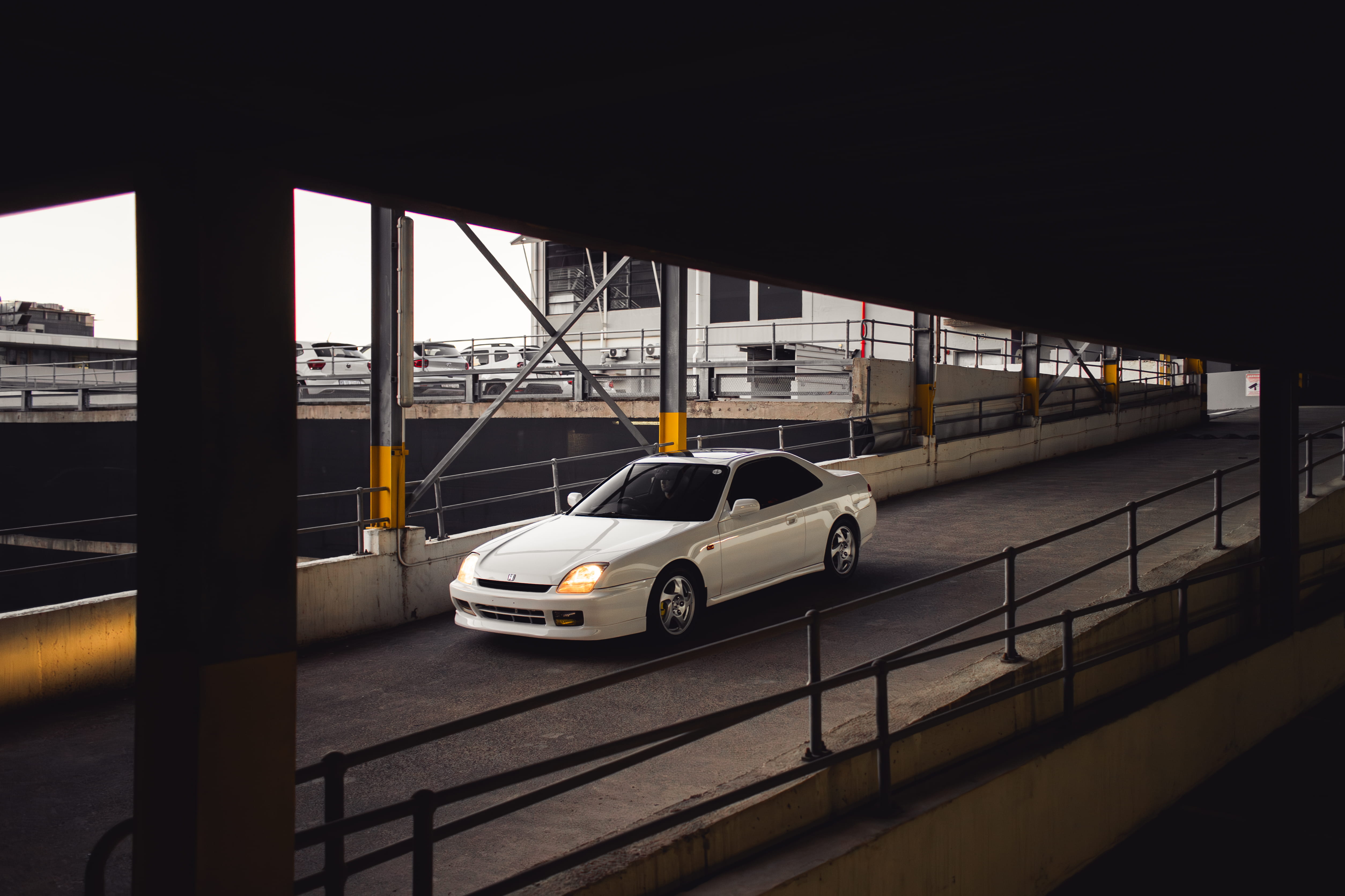A white Honda Prelude driving up a parking garage ramp.